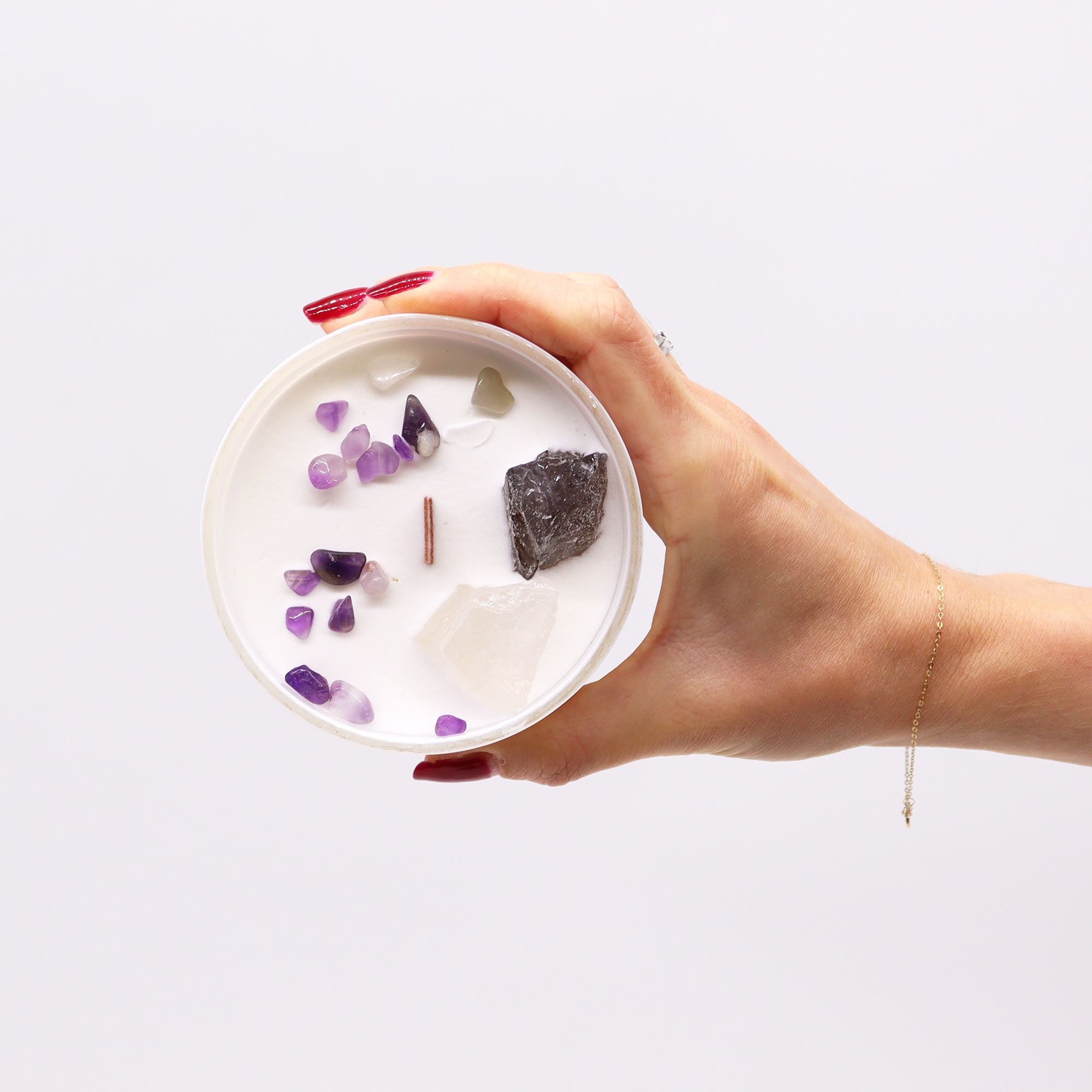 Hand holding a small round dish with crystals on a white background