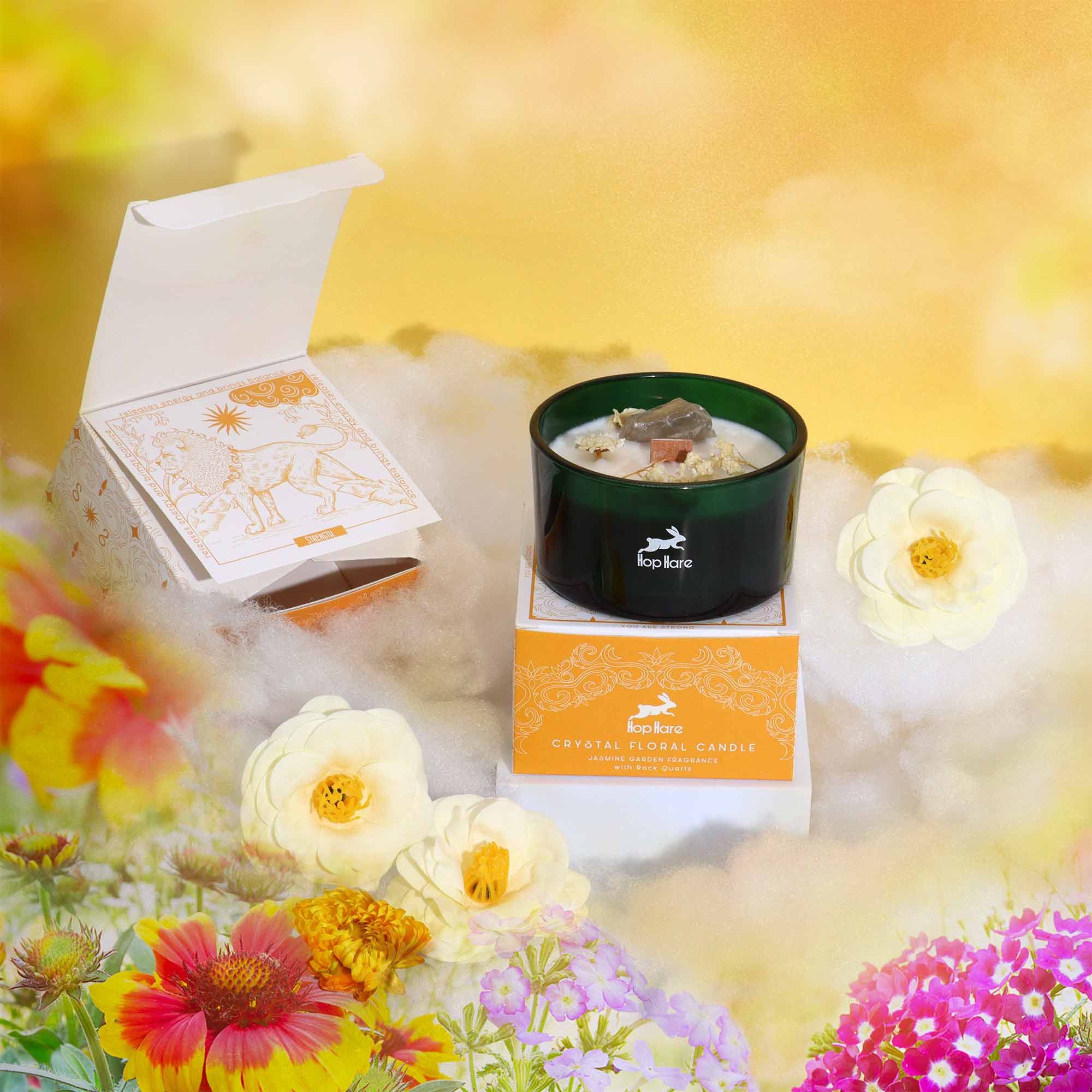 A candle displayed with a tarot card and orange gift box among bright flowers and golden clouds.