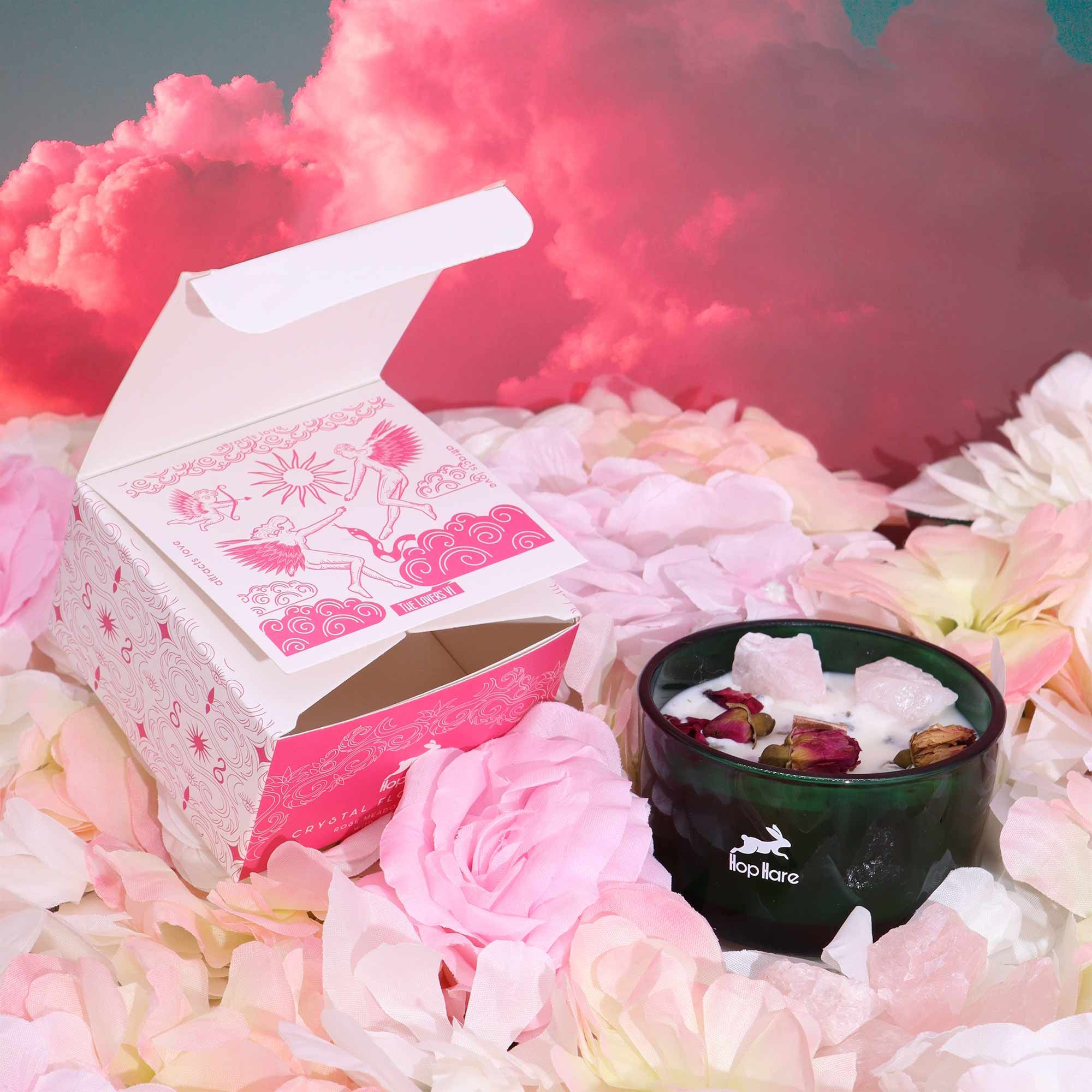 Product packaging with a candle on a bed of flowers against a pink smoke background