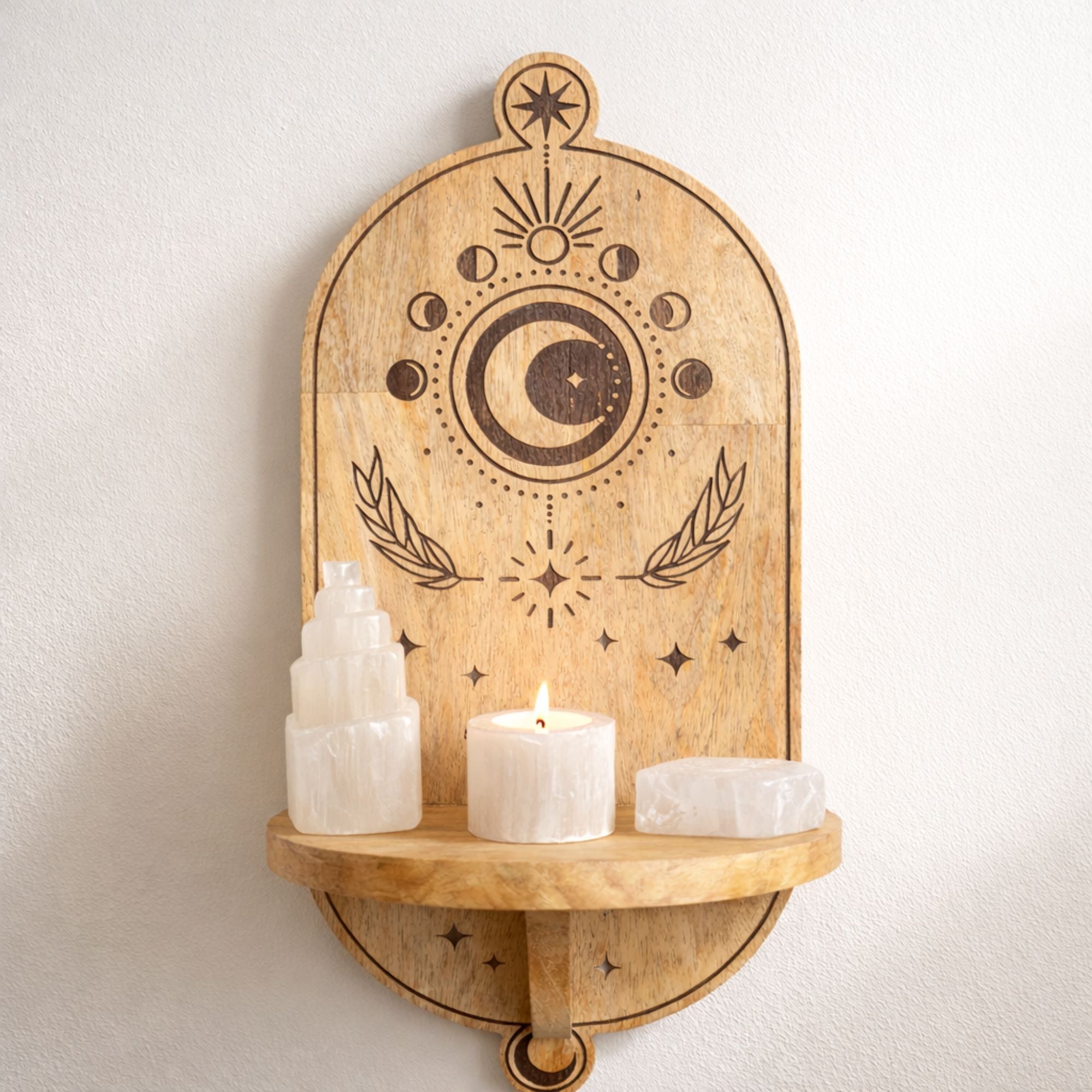 Wooden wall shelf with celestial design, candles, and crystals on a white wall.