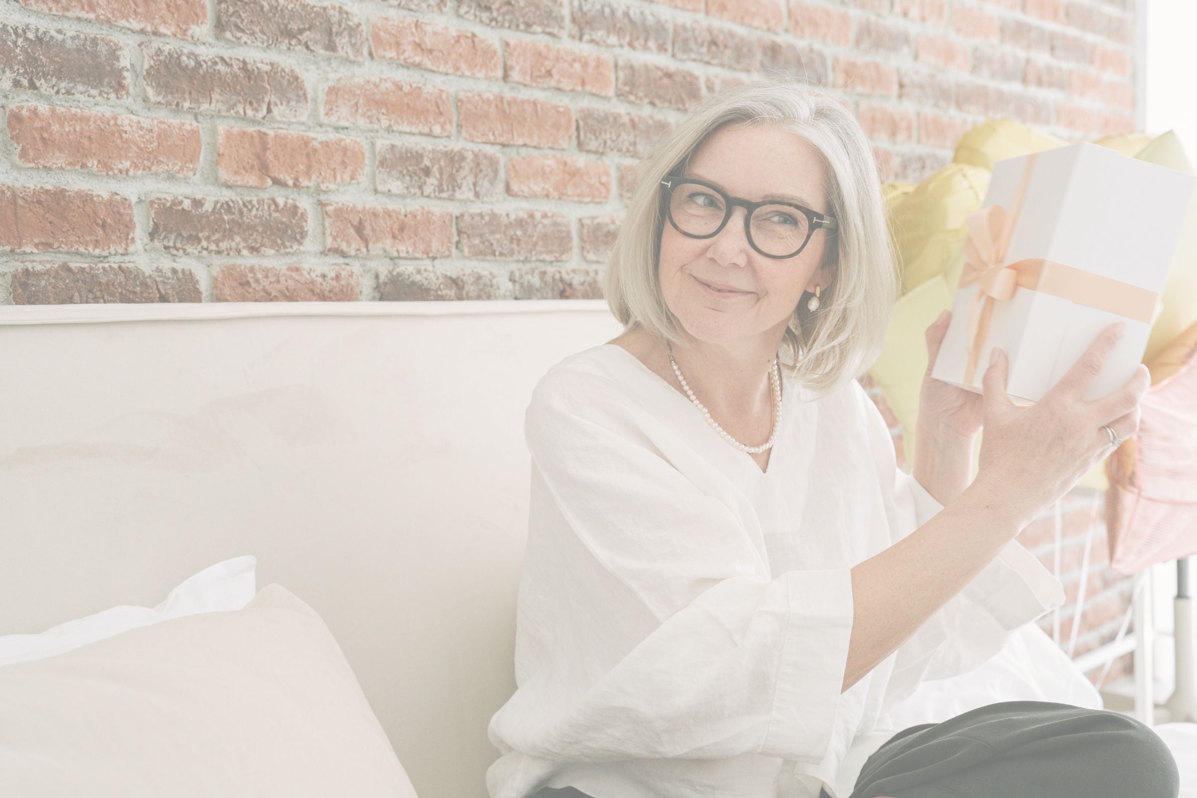 Woman sitting on a couch holding a wrapped gift against a brick wall.