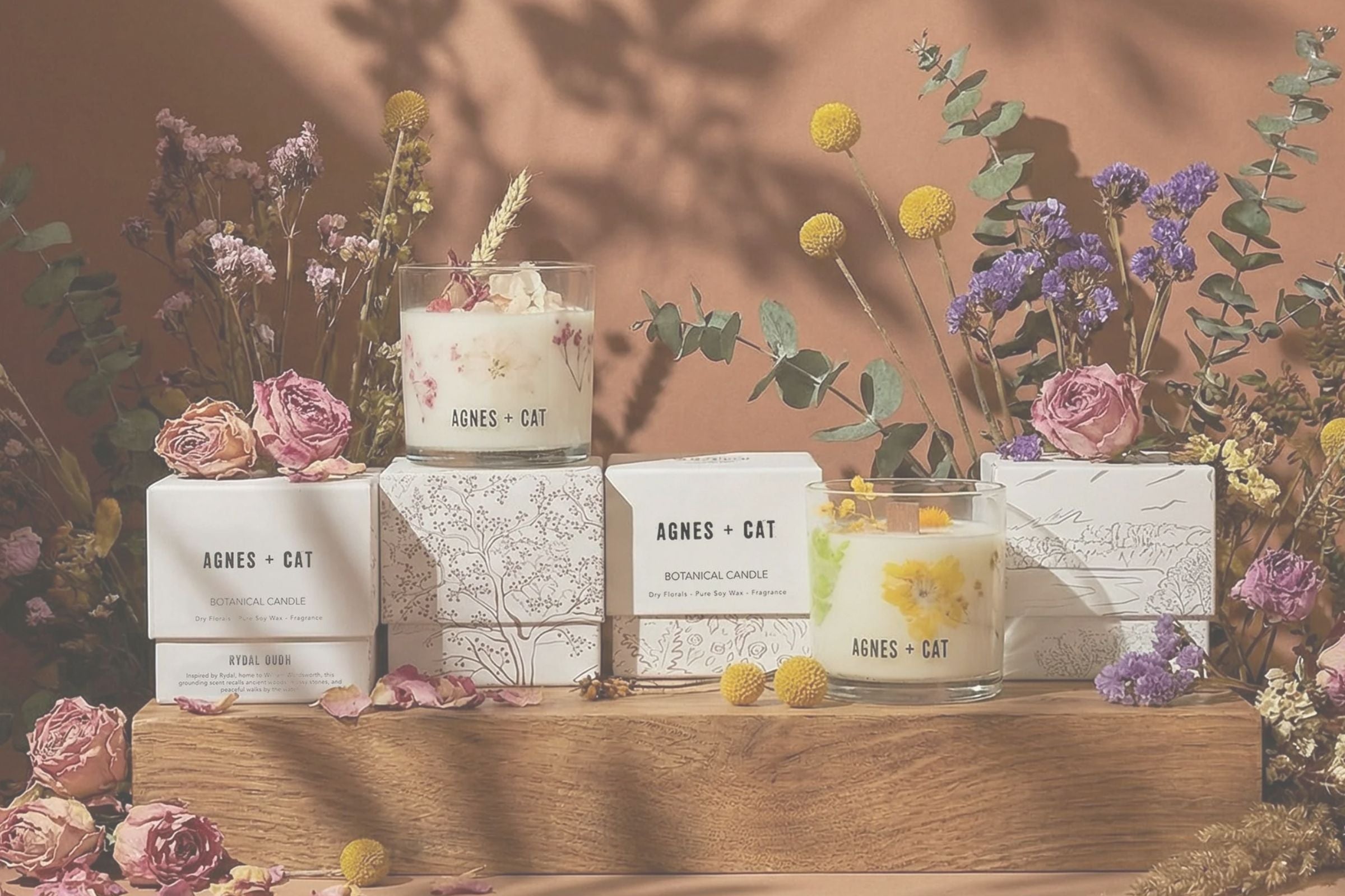Candles and boxes with 'AGNES & CAT' branding on a wooden surface with flowers.