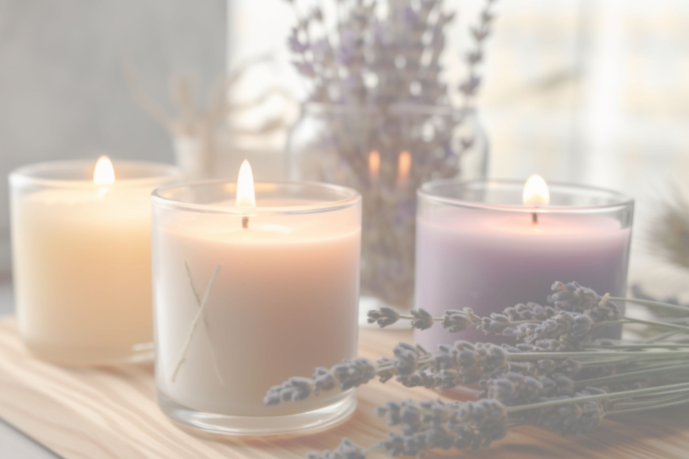 Three lit candles on a wooden surface with lavender flowers in the background