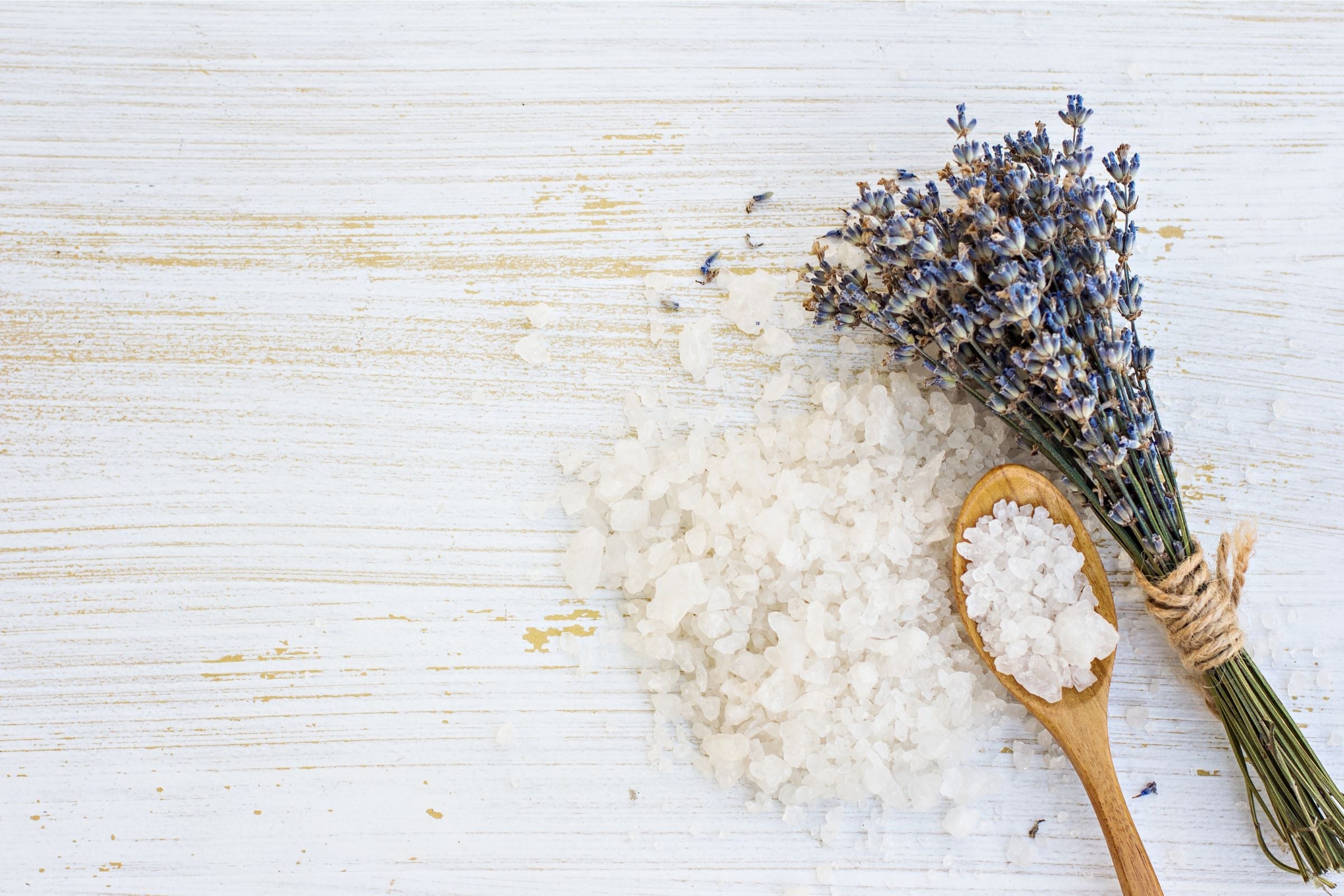 Wooden spoon with bath salt and lavender flowers on a wooden surface