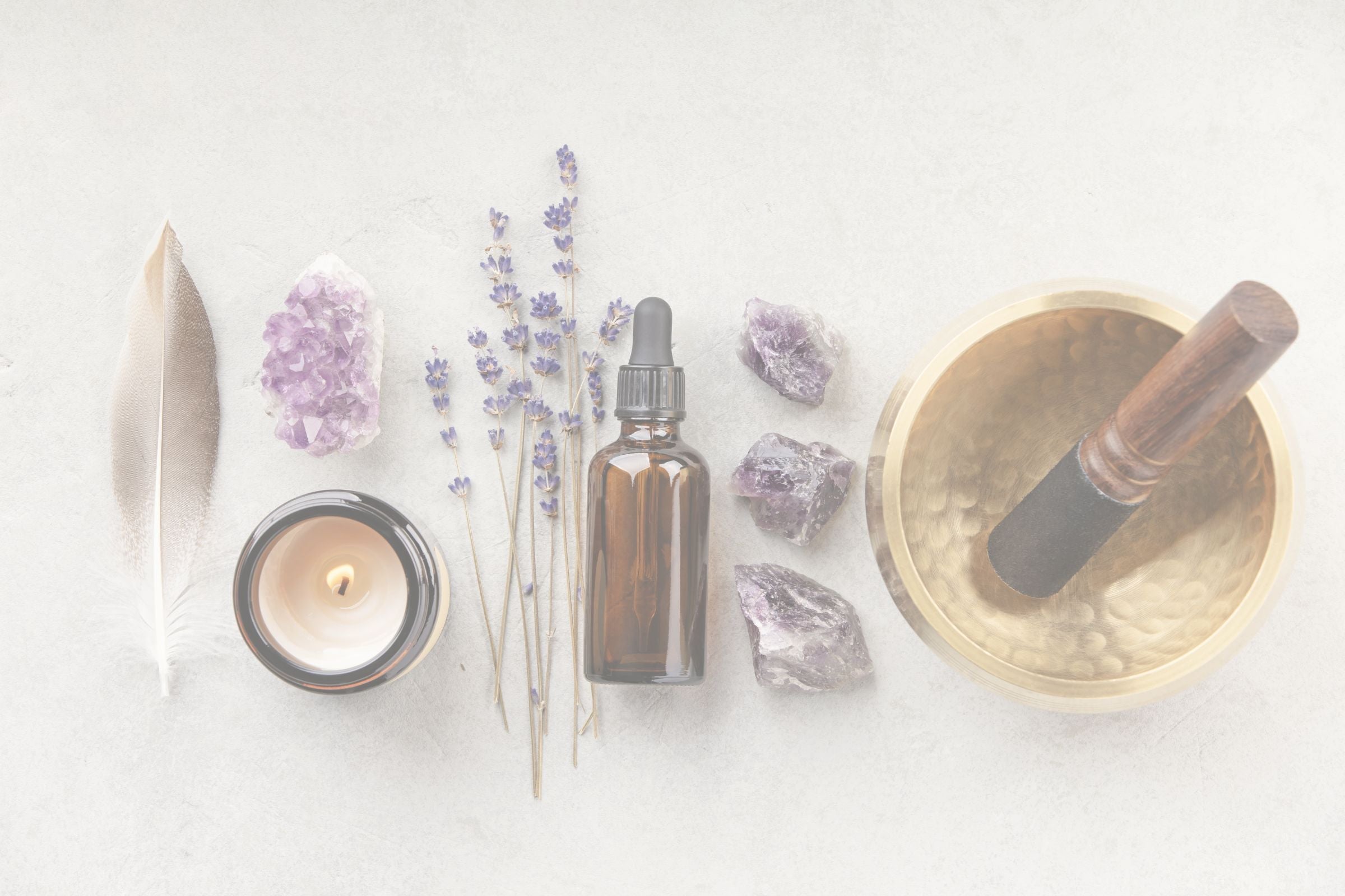A still-life arrangement of a candle, crystals, a bottle, and a singing bowl on a white surface.