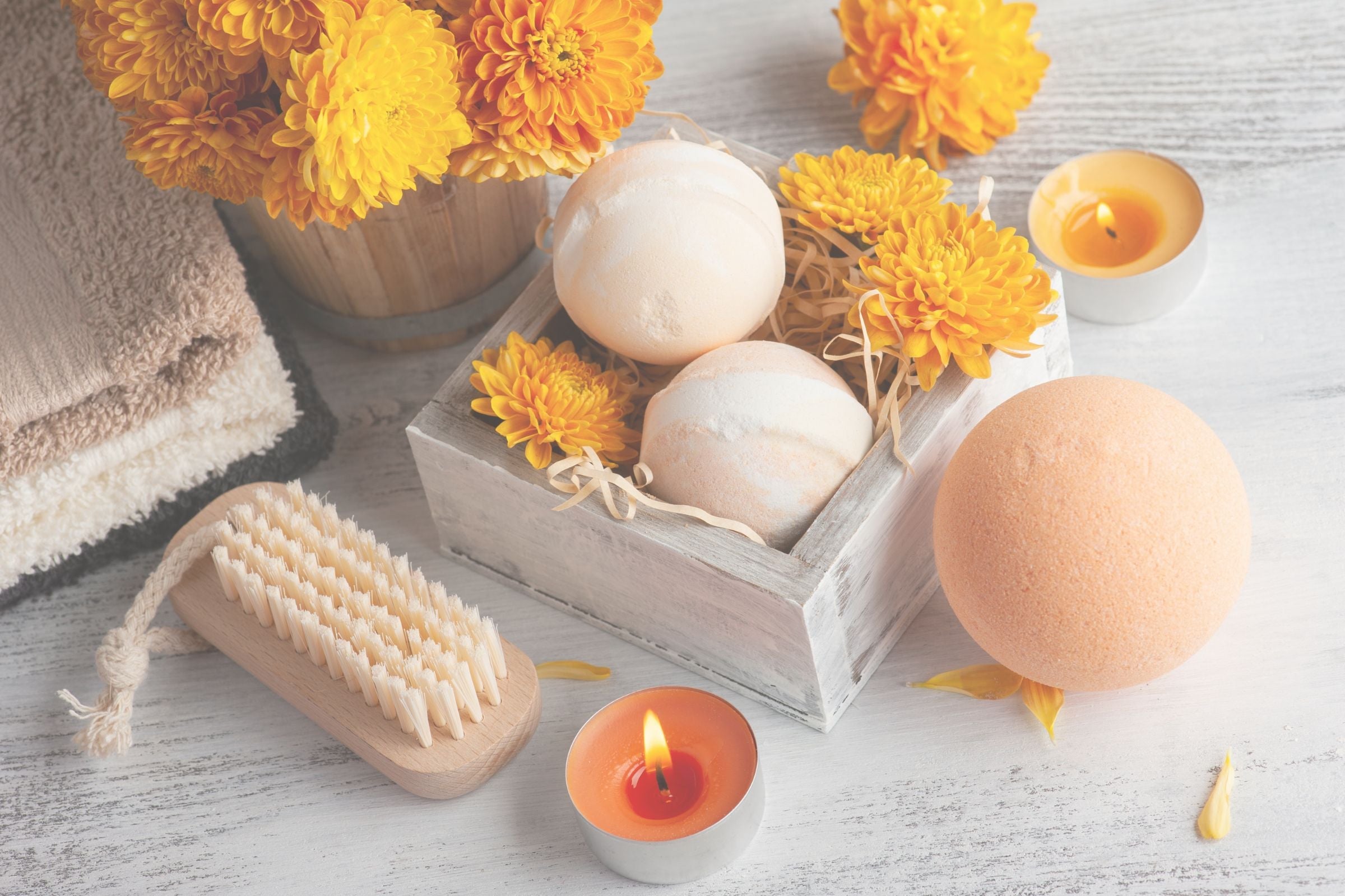 Bath bombs, a brush, and candles on a wooden surface with yellow flowers.