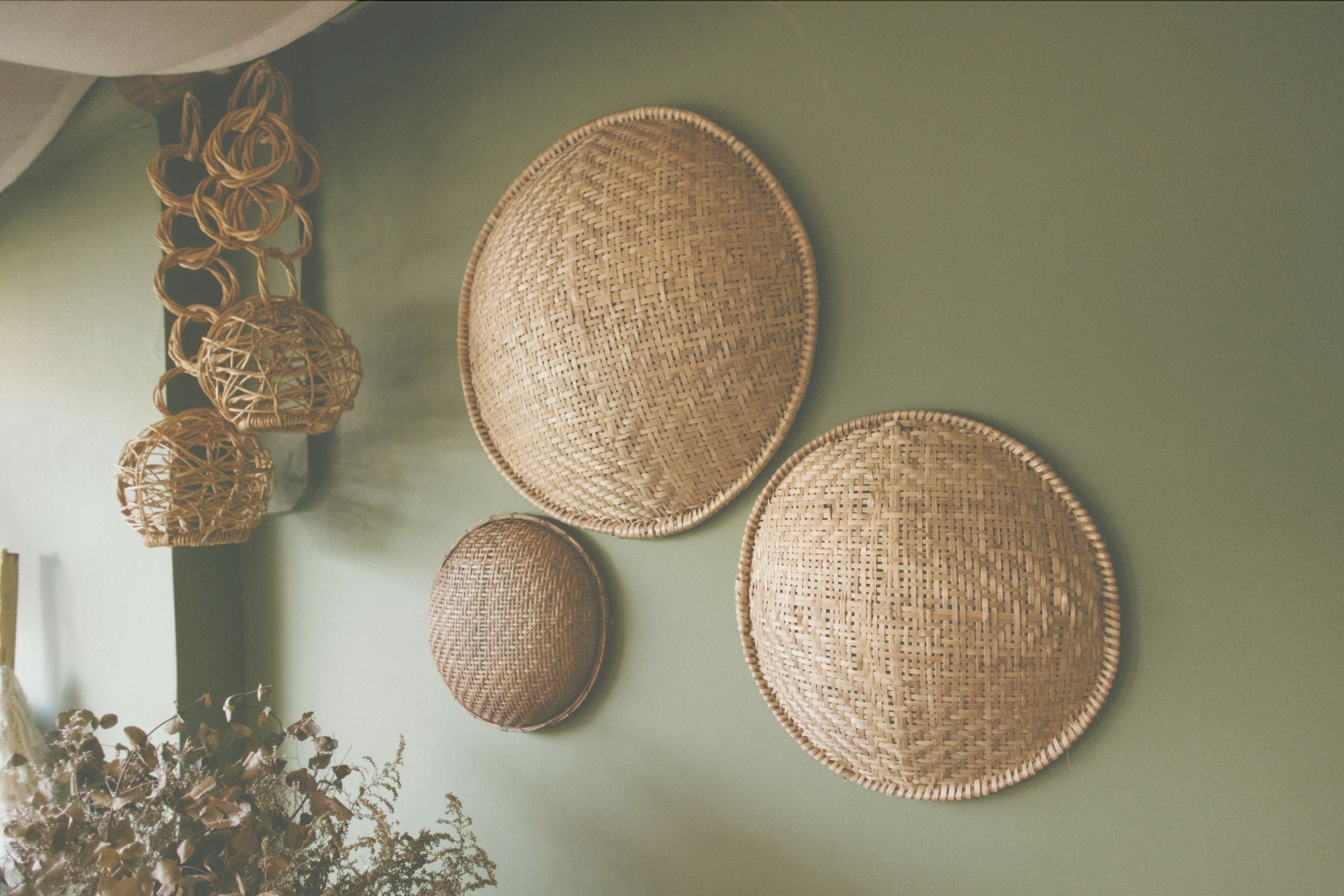 Three woven baskets of different sizes on a light green wall.
