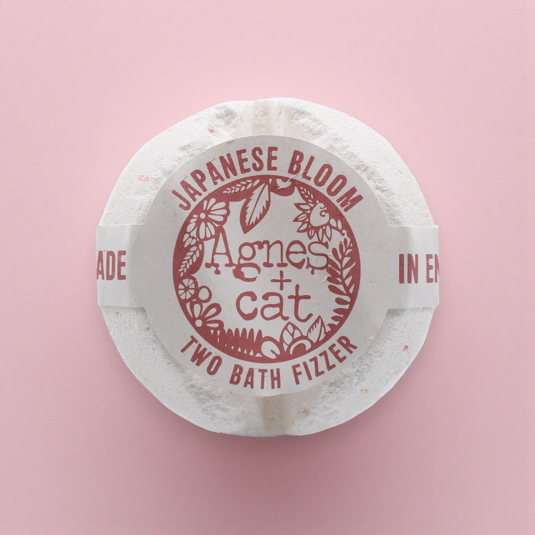 Round white bath fizzer with red text on a pink background