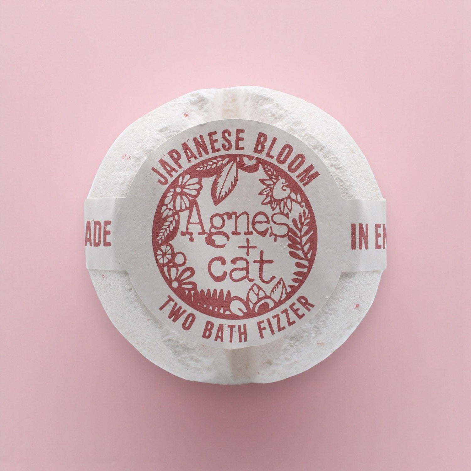 Round white bath fizzer with red text on a pink background