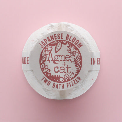 Round white bath fizzer with red text on a pink background