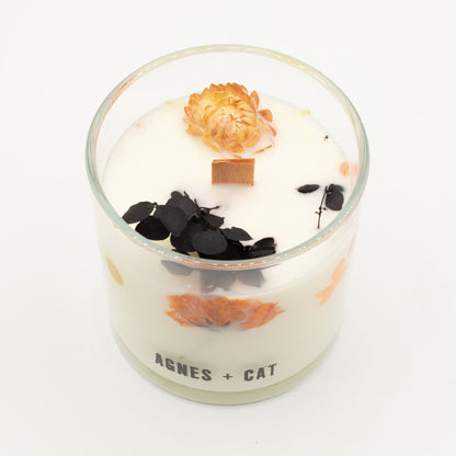 Decorative candle with flowers and leaves in a glass container on a white background