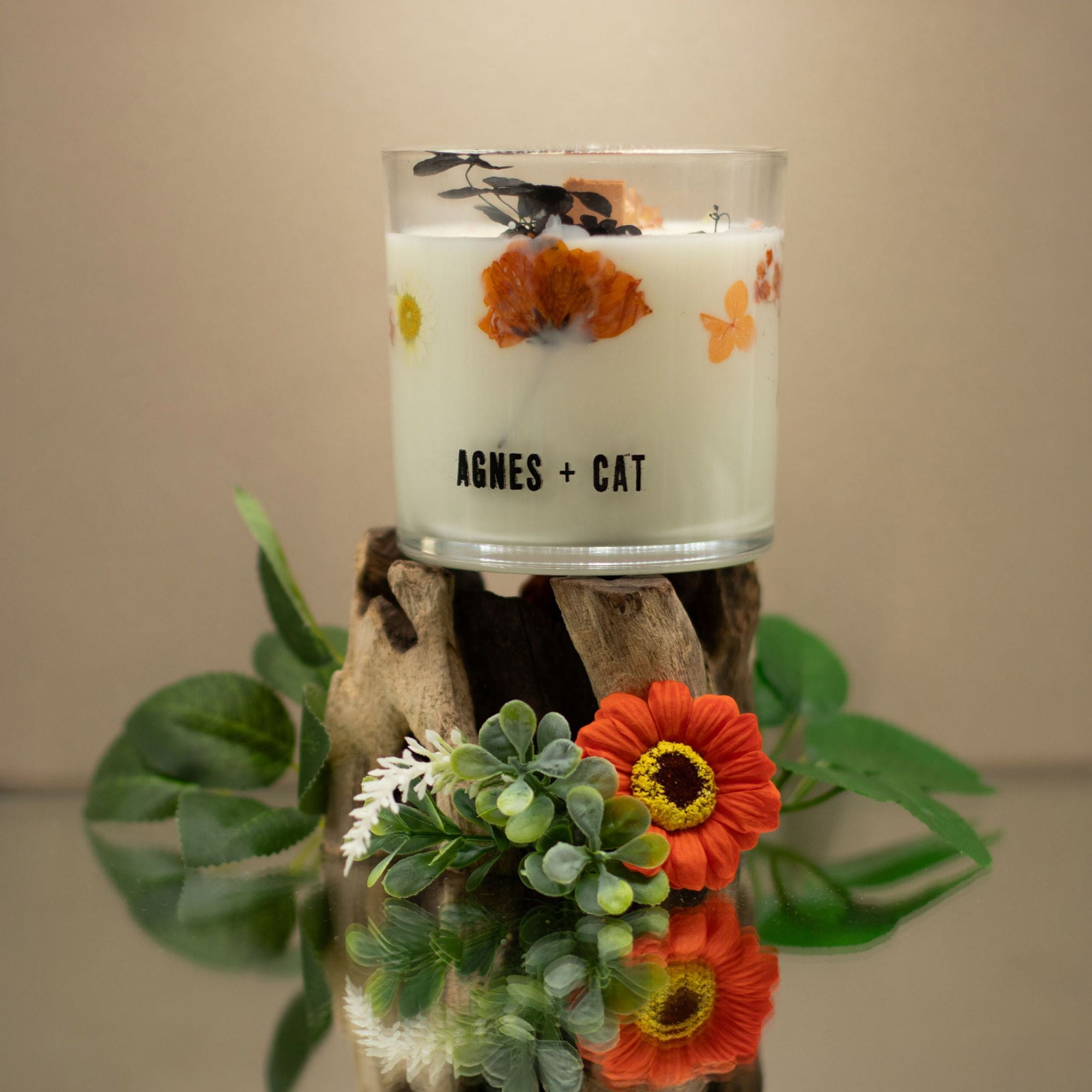 Candle in a glass jar with floral design on a wooden block, featuring the brand &