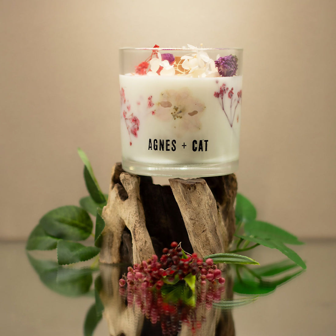 A candle in a glass holder with a floral design on a wooden stand, featuring the brand &