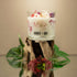 A candle in a glass holder with a floral design on a wooden stand, featuring the brand &