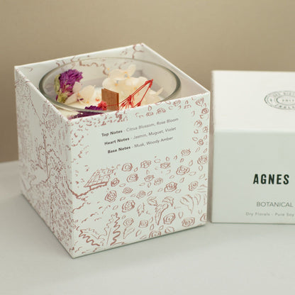 A candle in a decorative box with a floral design, featuring the brand &