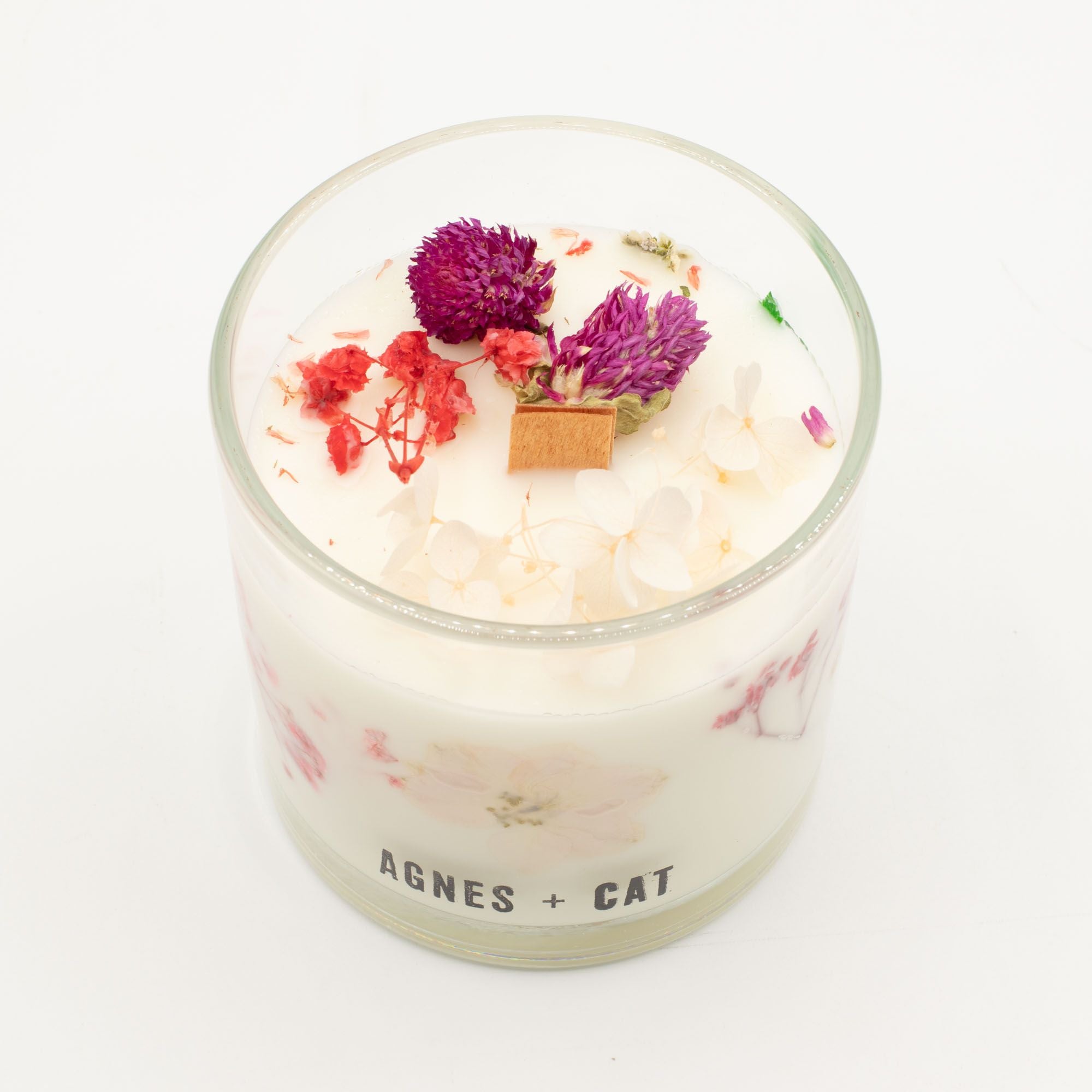 A candle with dried flowers in a glass container on a white background, branded &