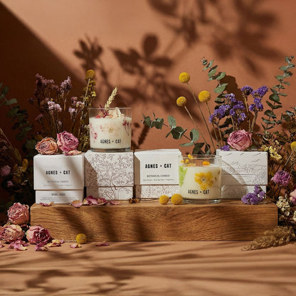 Candles with floral packaging on a wooden stand against a warm brown background