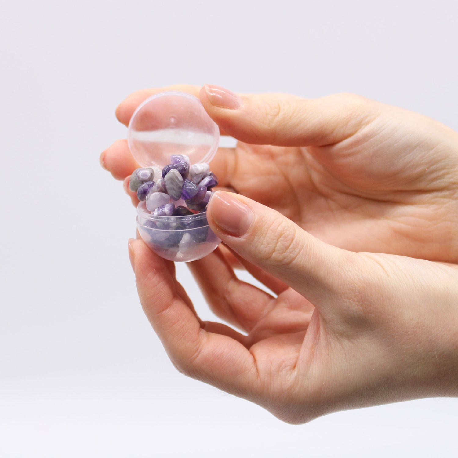 Hand holding a small transparent container filled with a purple bracelet against a light gray background