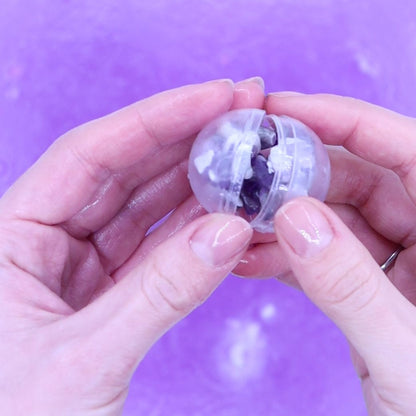 Clear plastic ball with a purple bracelet inside, held between two hands against a purple background