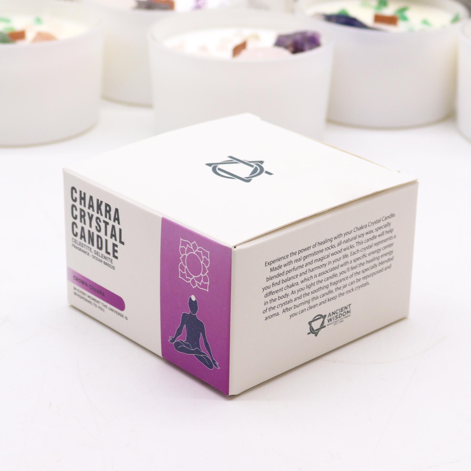 Box of Chakra Crystal Candle on a white surface with blurred candles in the background