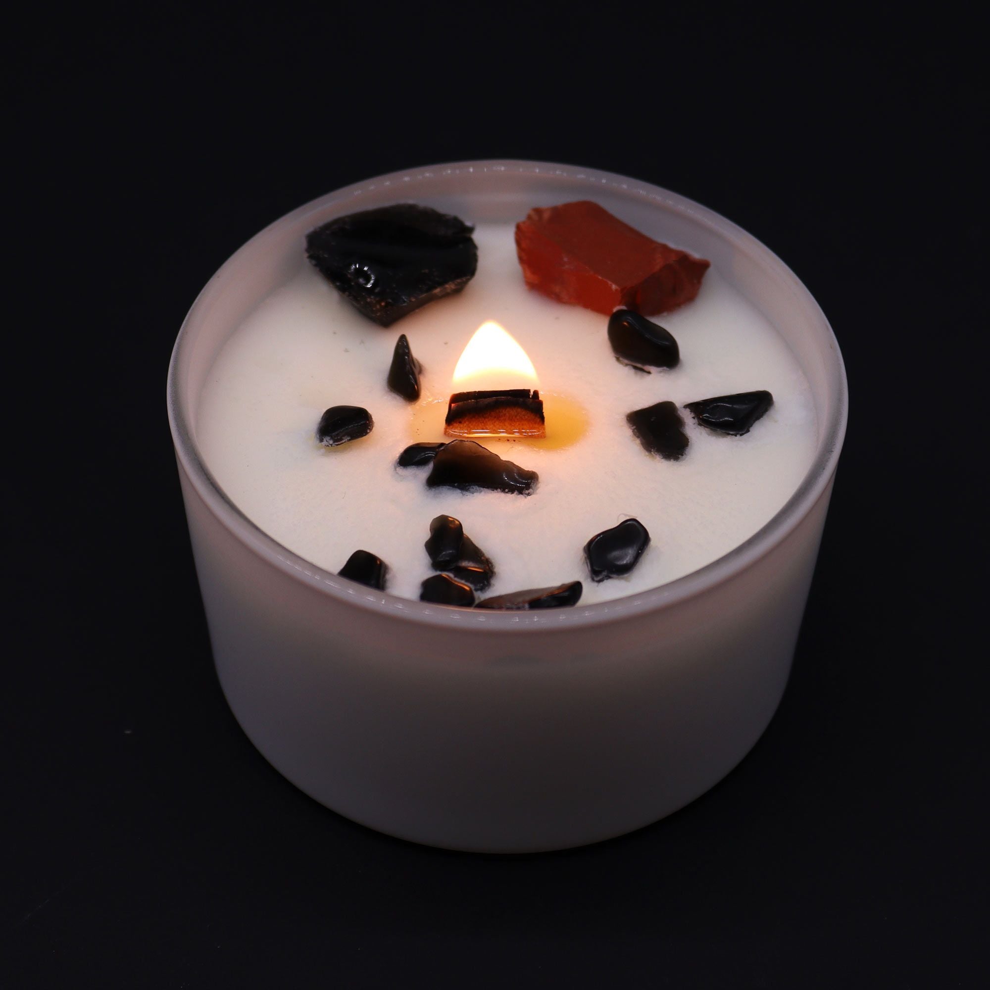 Candle with dark pieces on top against a black background