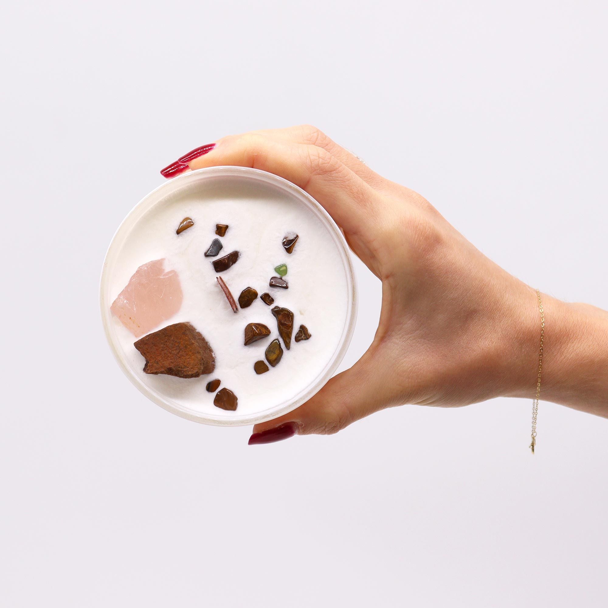 Hand holding a candle with chocolate-coloured stones on a light gray background