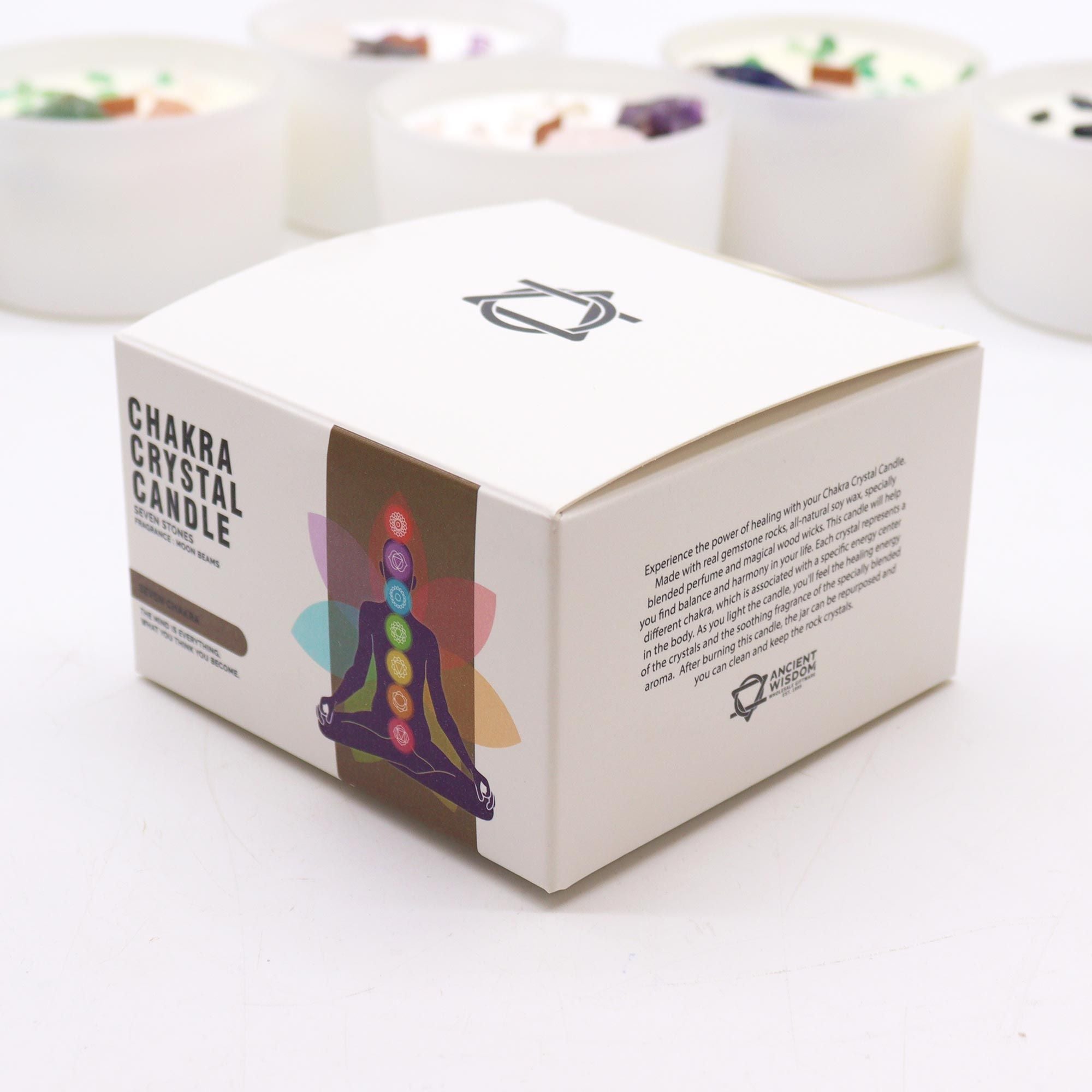 Box of Chakra Crystal Candle on a white surface with blurred candles in the background