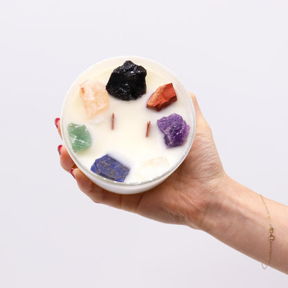 Hand holding a Seven Chakra Crystal Candle with colorful stones on a light grey background