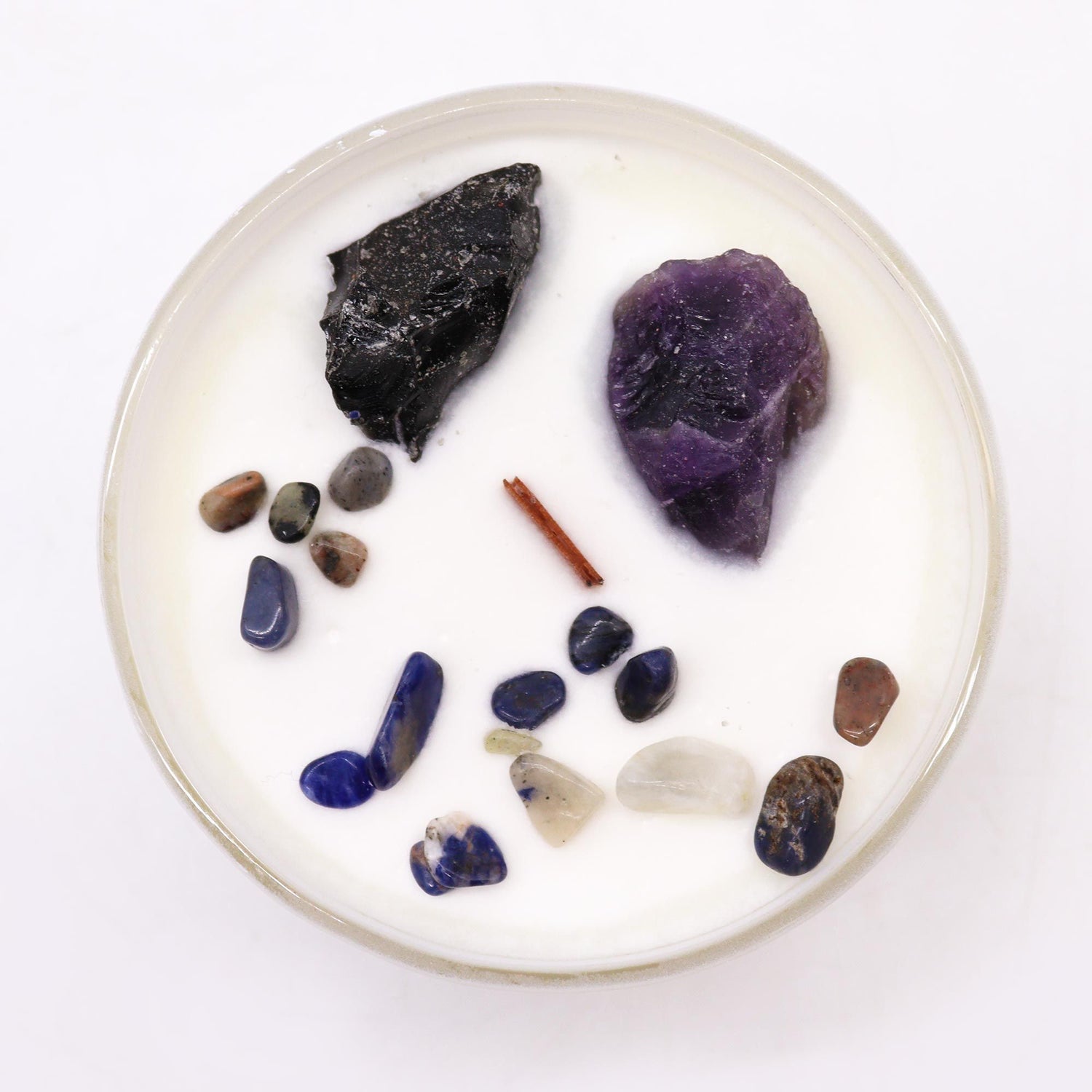 Round white candle with assorted stones and a stick on a white background