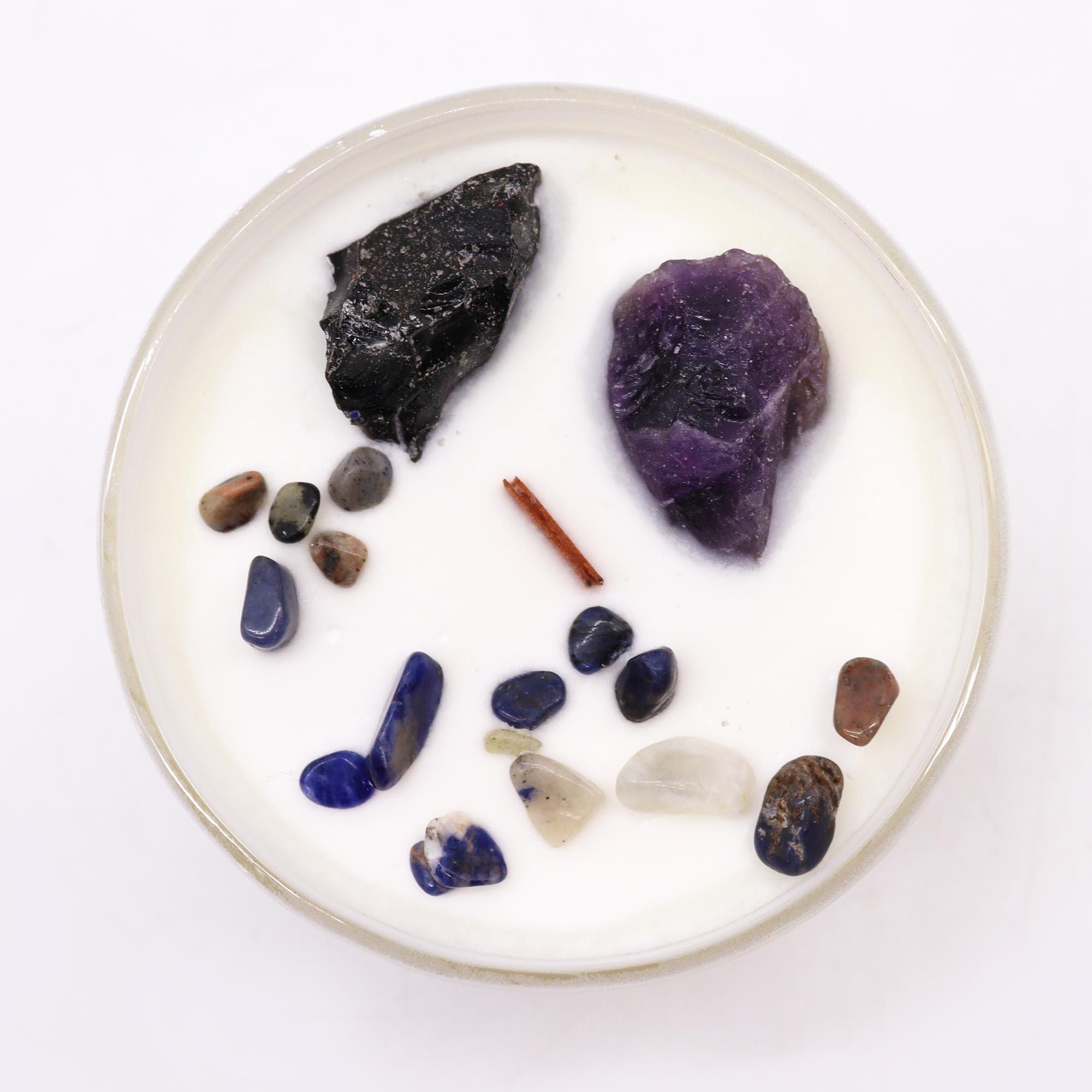 Round white candle with assorted stones and a stick on a white background