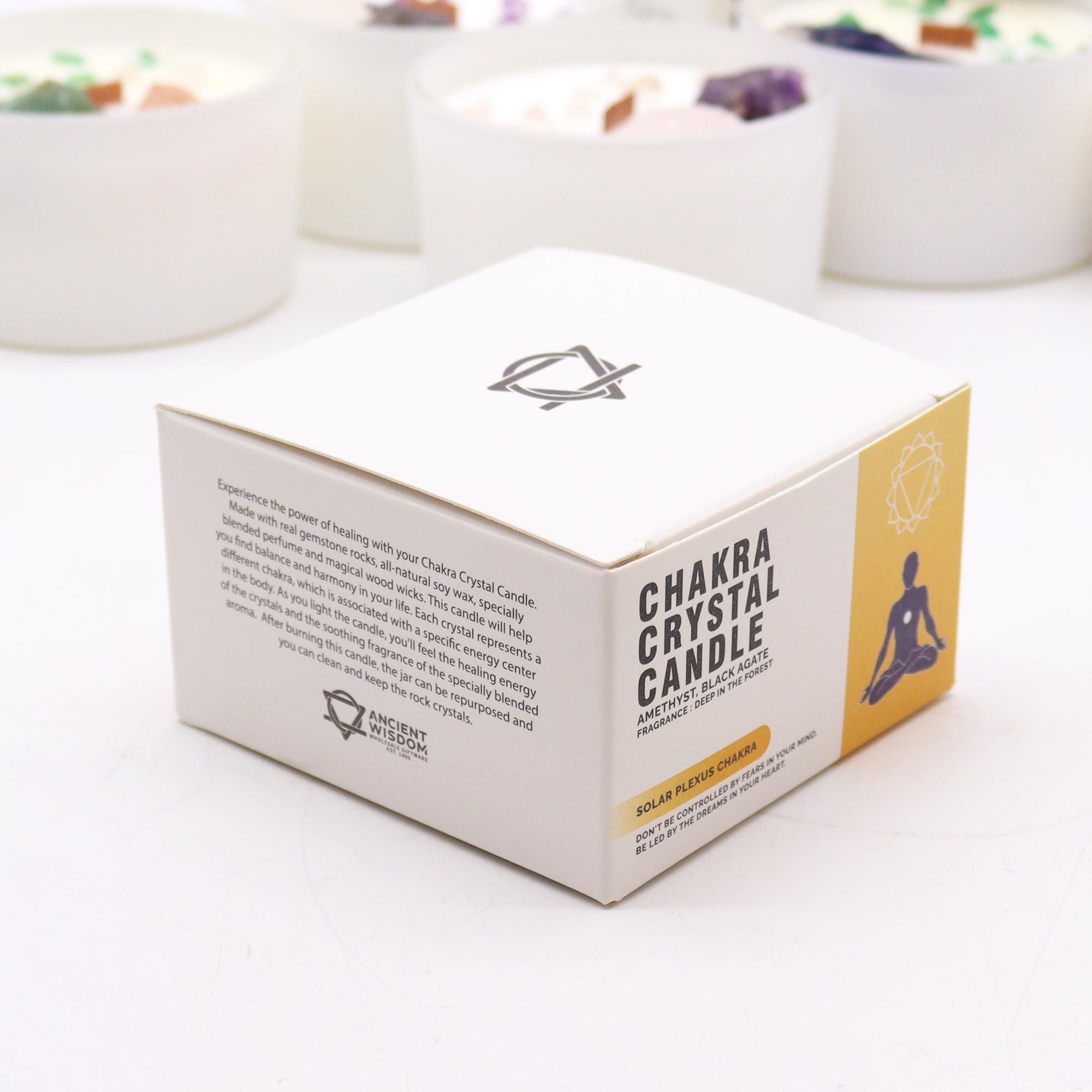 Box of Chakra Crystal Candle on a white surface with blurred candles in the background