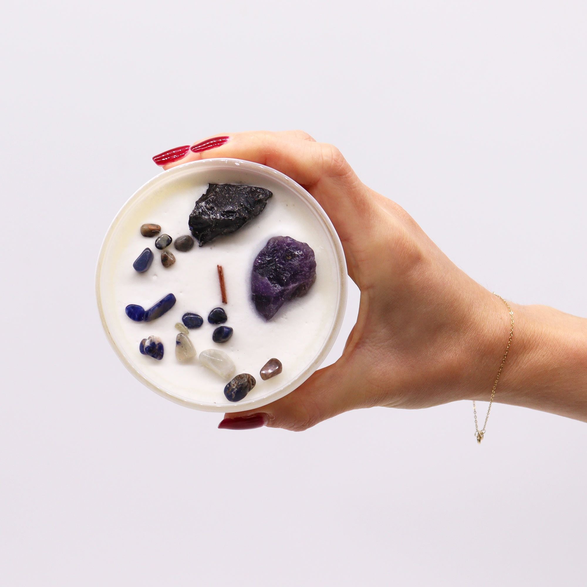 Hand holding a bowl with various stones and crystals on a white background