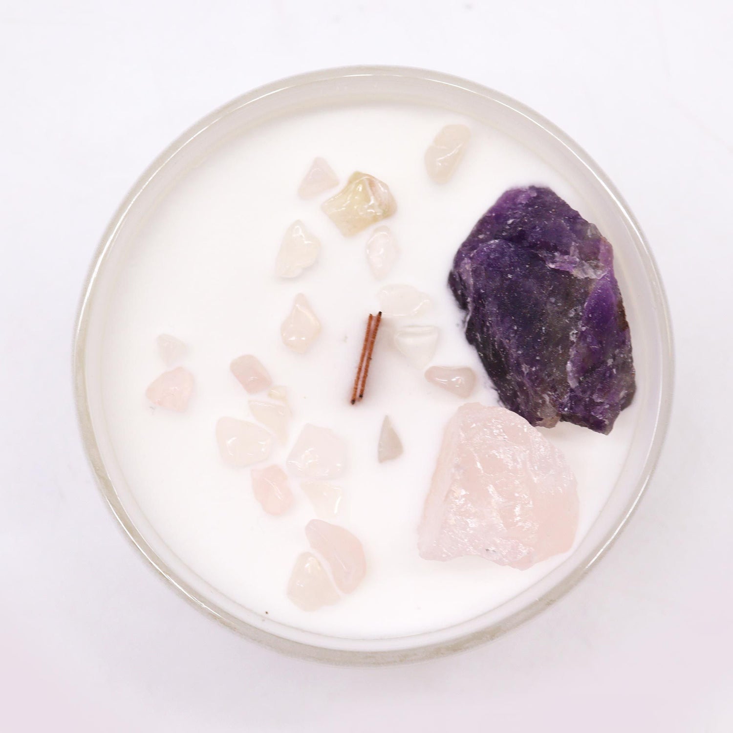 Candle with natural stones and a purple crystal on a white background
