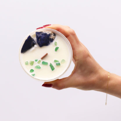 Hand holding a container with a candle inside, featuring decorative stones on a white background