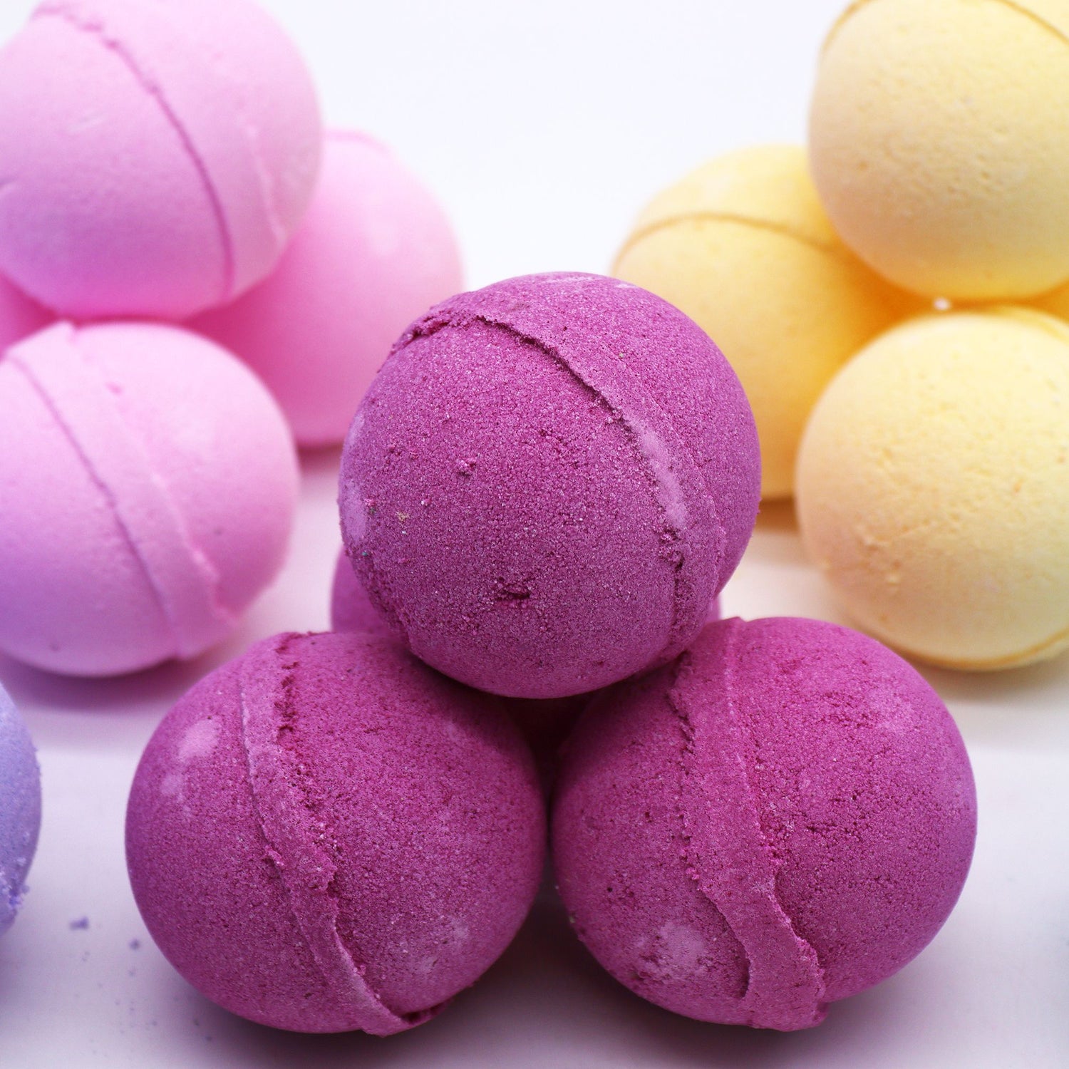 Colorful bath bombs in purple, pink, and yellow on a light background