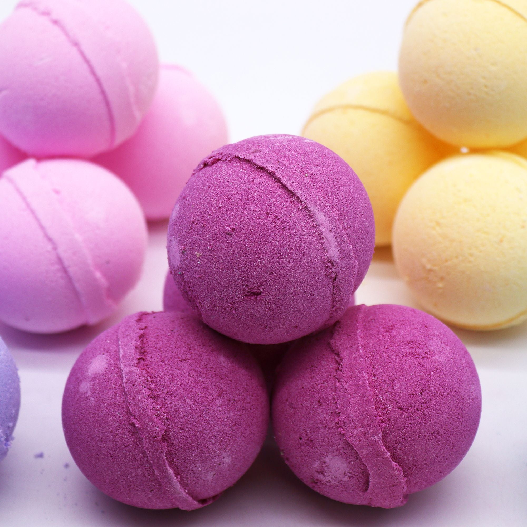 Colorful bath bombs in purple, pink, and yellow on a light background