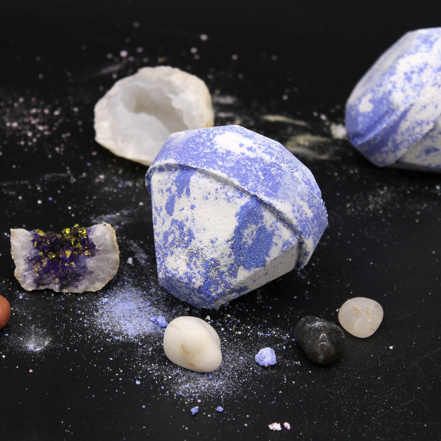 Blue and white marbled bath bomb on a black surface with small rocks and crystals.