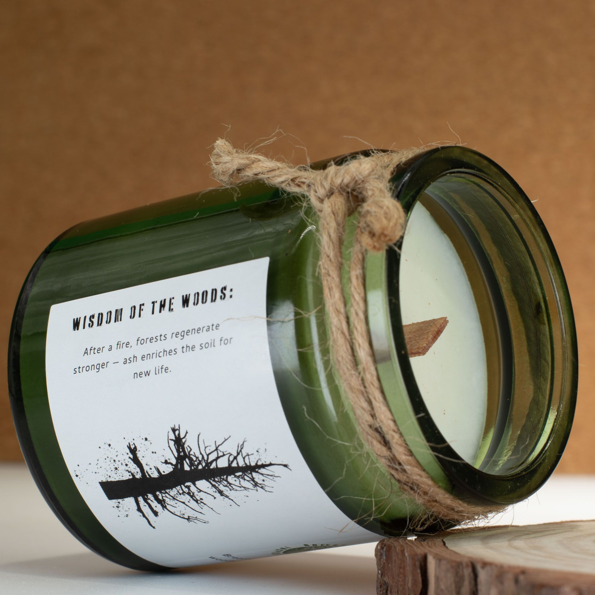 Candle in a green glass jar with a label and twine, on a wooden surface with a brown background.