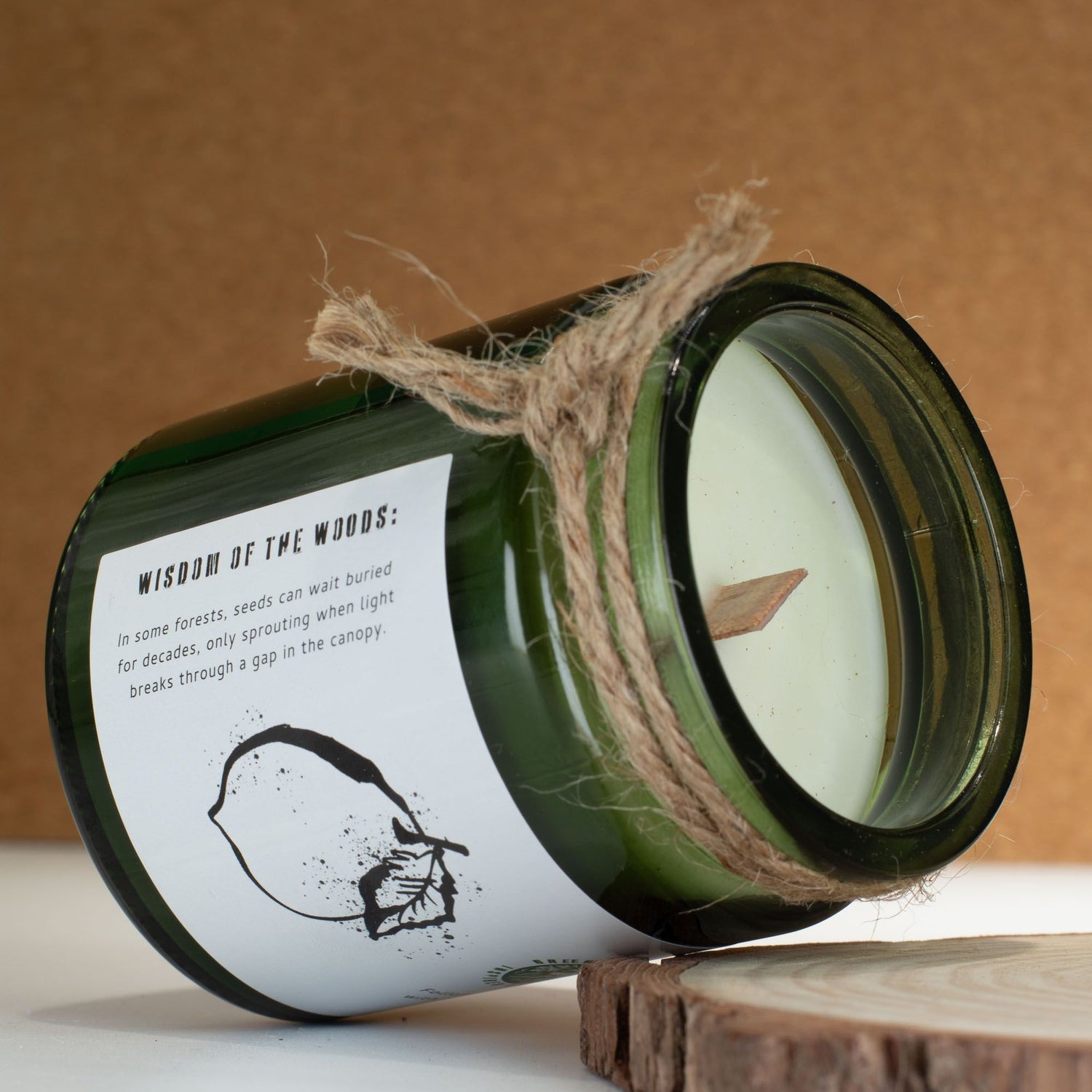 Green candle in a glass jar with a label and twine, on a wooden surface with a brown background.
