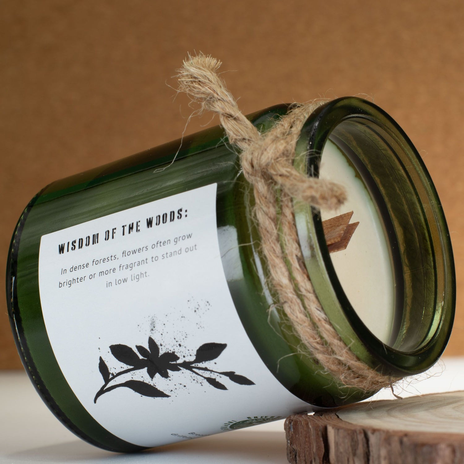 Green candle in a jar with a label and twine, placed on a wooden surface.