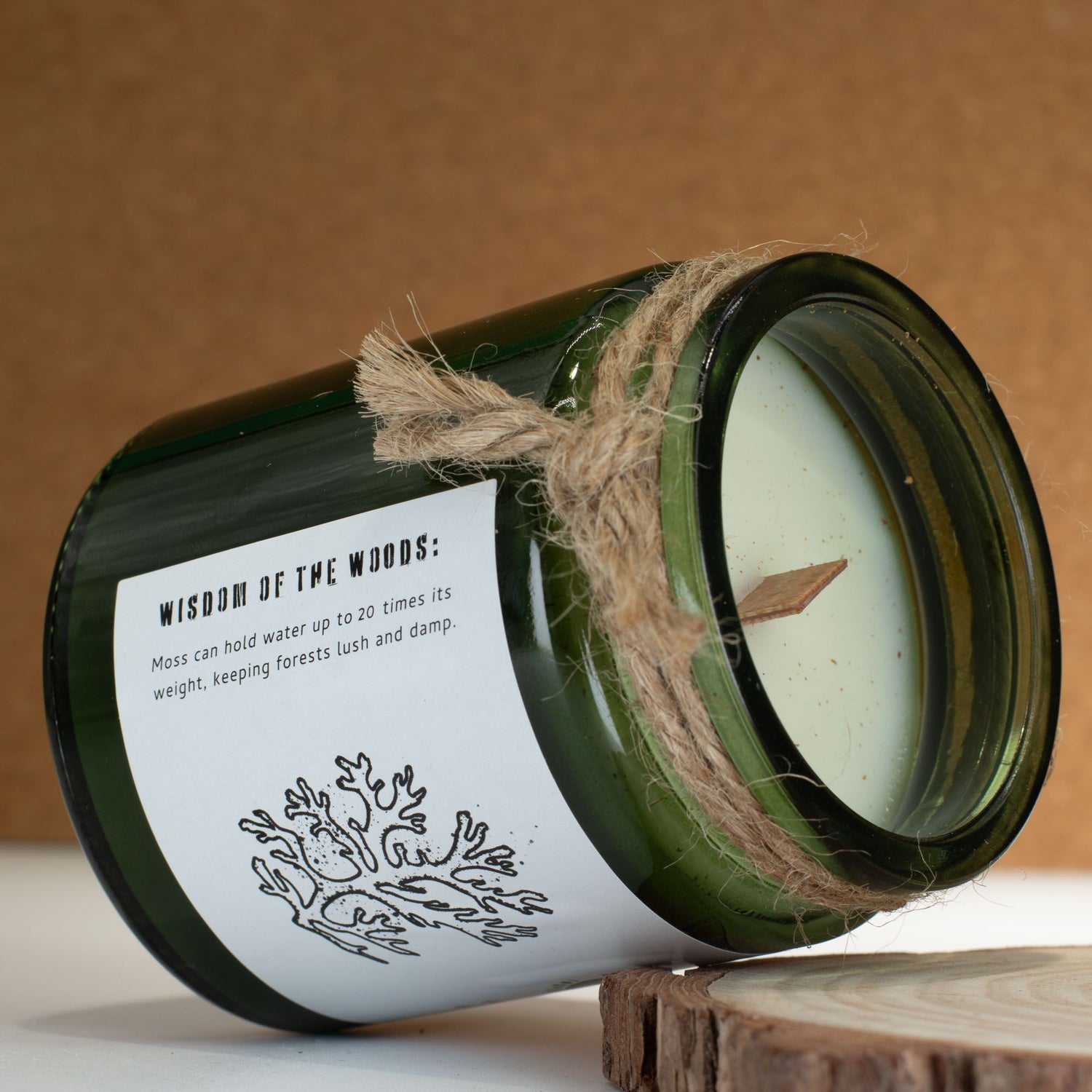 Green candle in a glass jar with a label and twine, on a wooden surface.