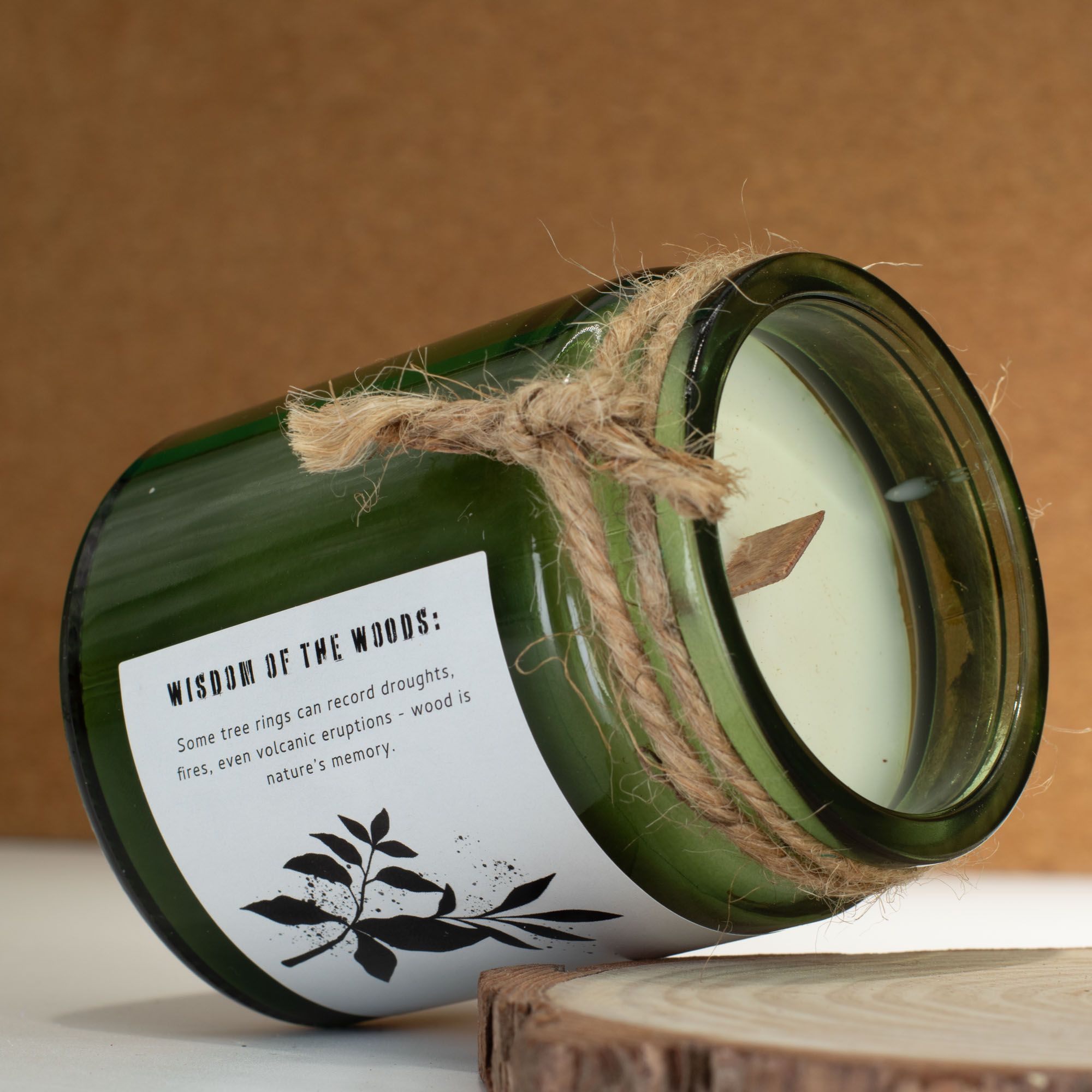 Green candle in a bottle with a label and twine on a wooden surface
