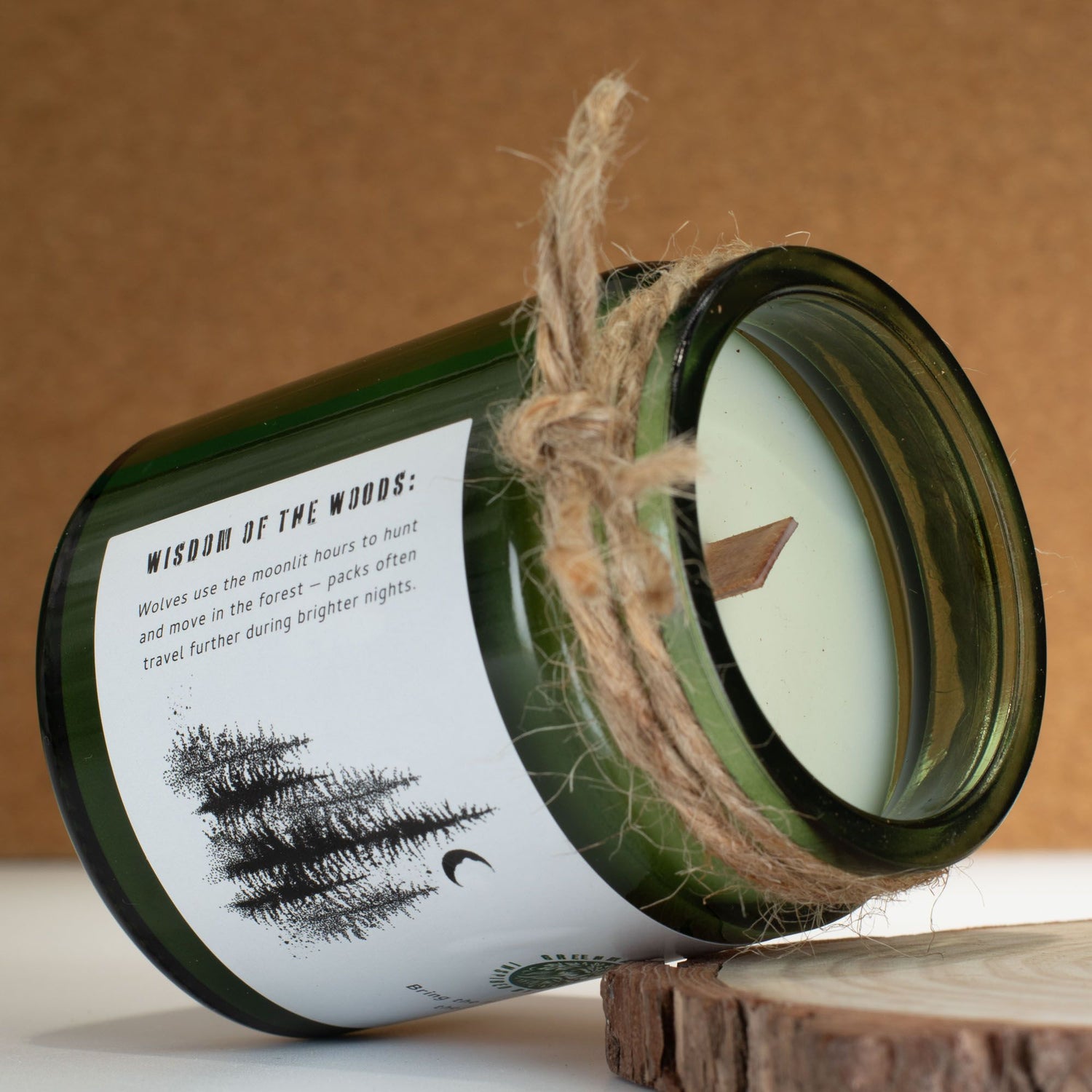 A candle in a green glass jar with a label and twine on a wooden surface.