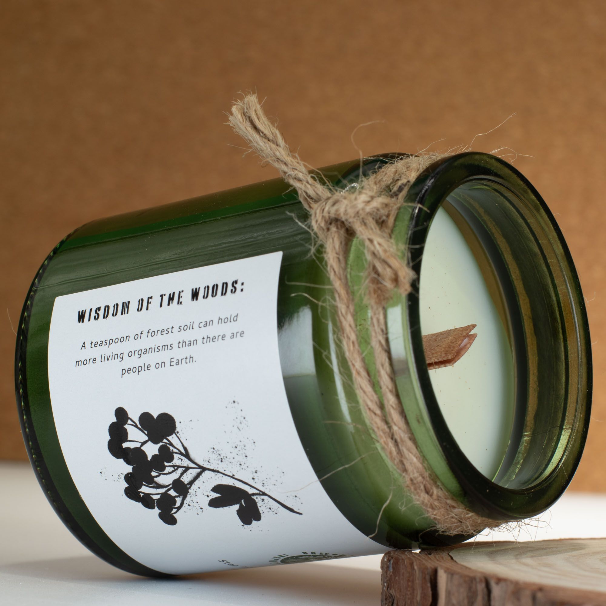 Candle in a green jar with a label and twine, on a wooden surface.