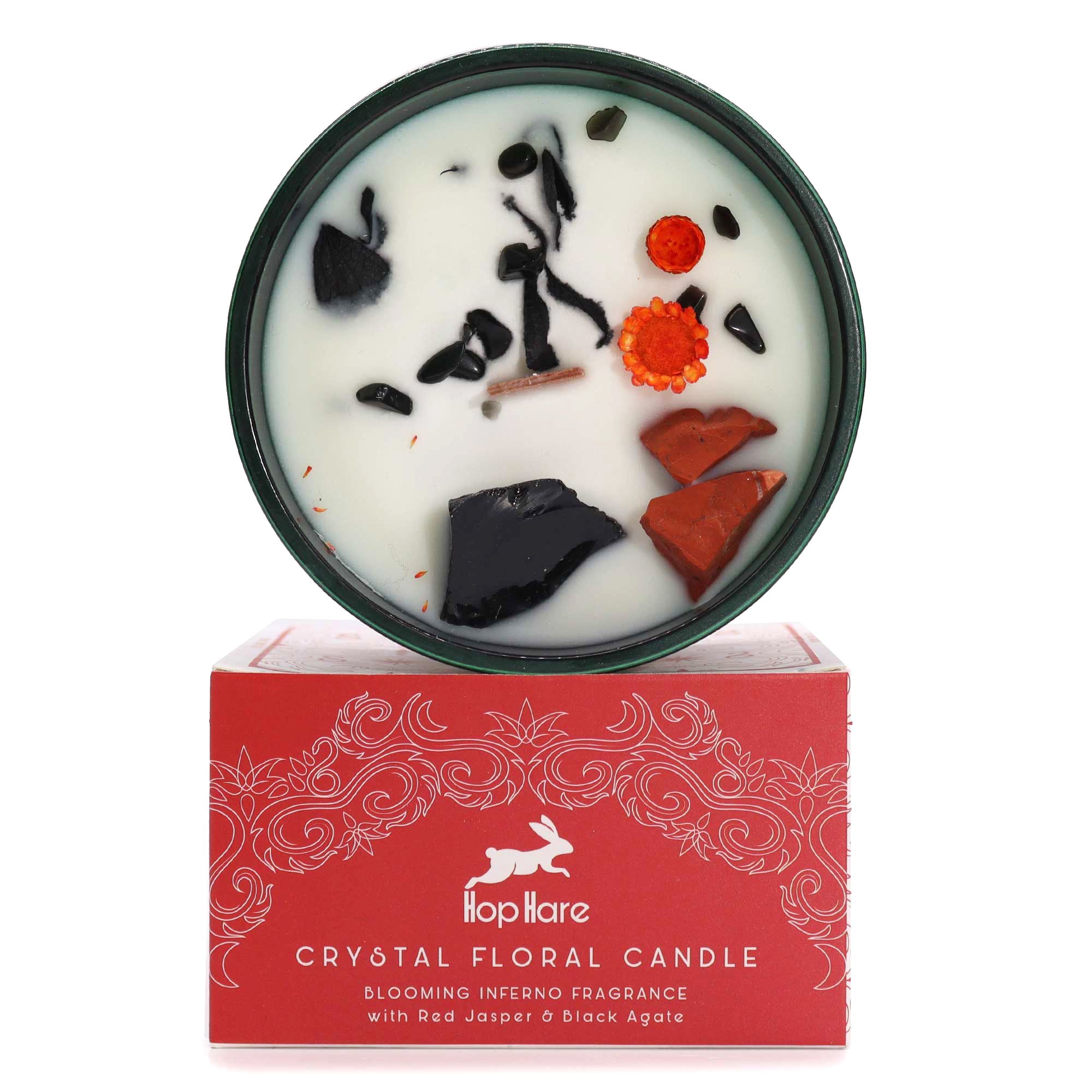 A candle in a dark green jar with red jasper, black agate gemstones and dried flowers on top of soy wax.