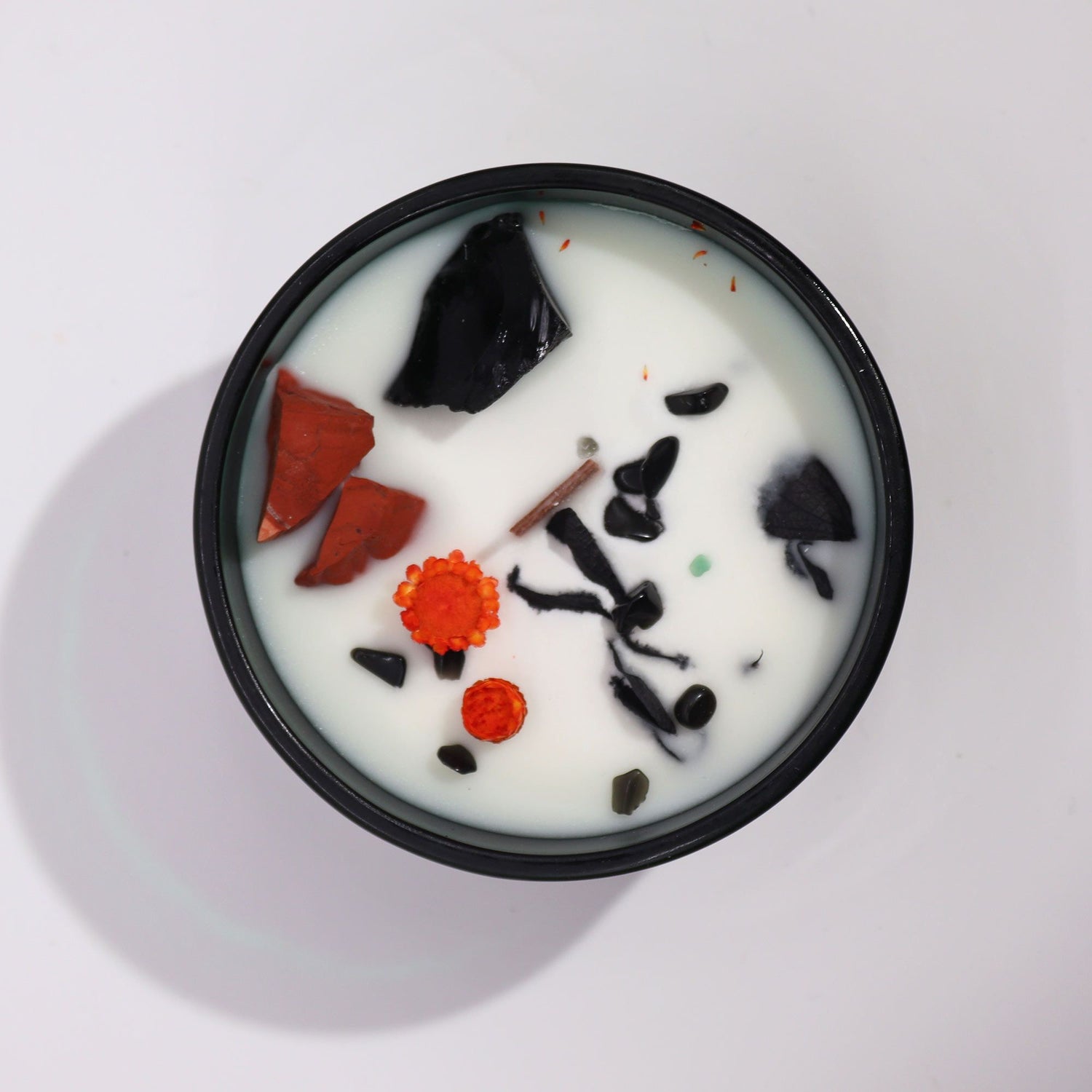 A white candle with black and red gemstones on a light gray background