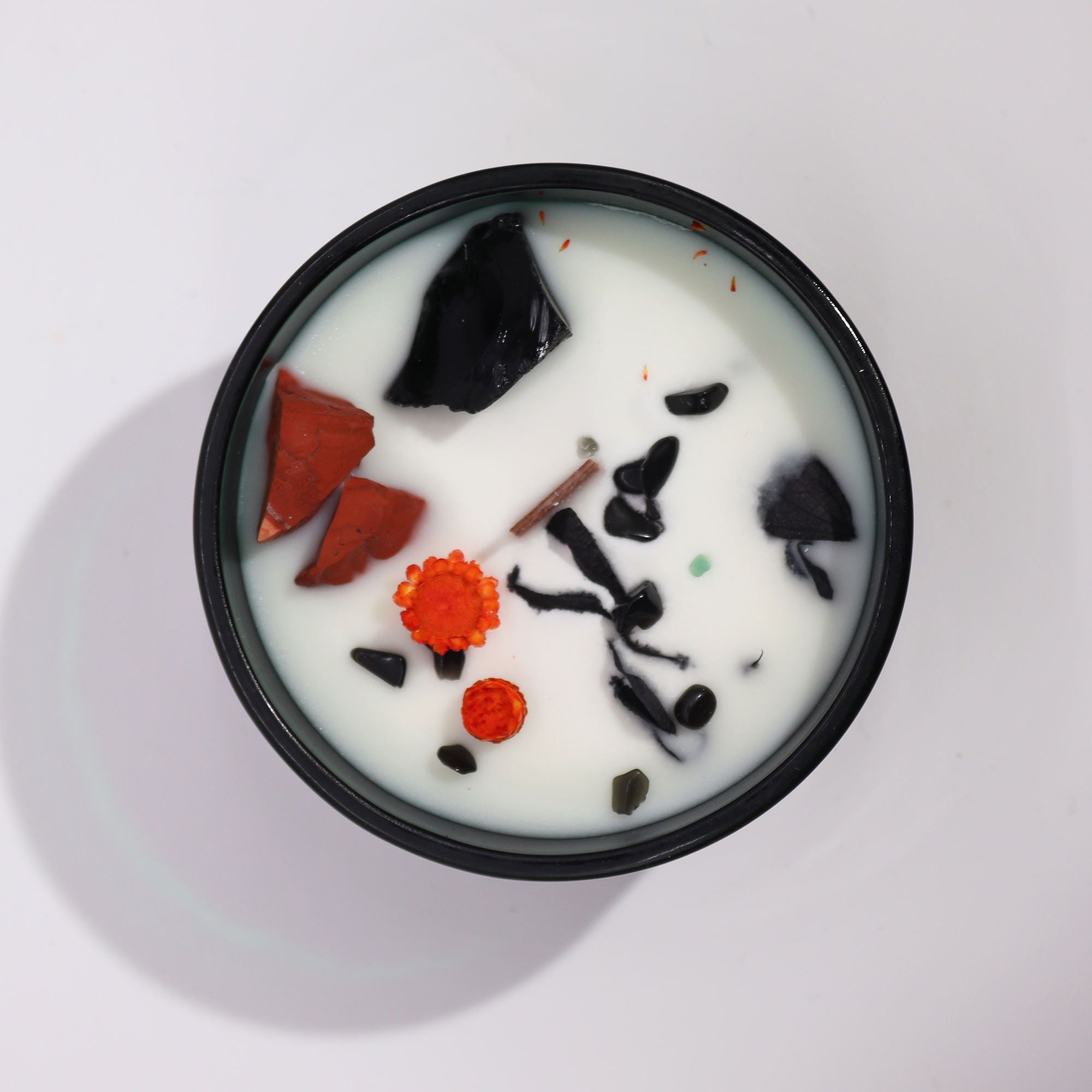 A white candle with black and red gemstones on a light gray background