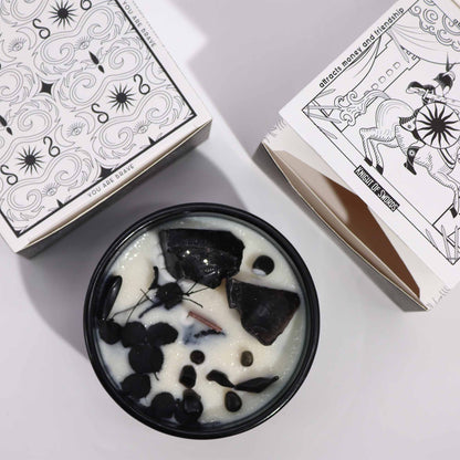 Candle with black and white design next to tarot card boxes on a light gray background