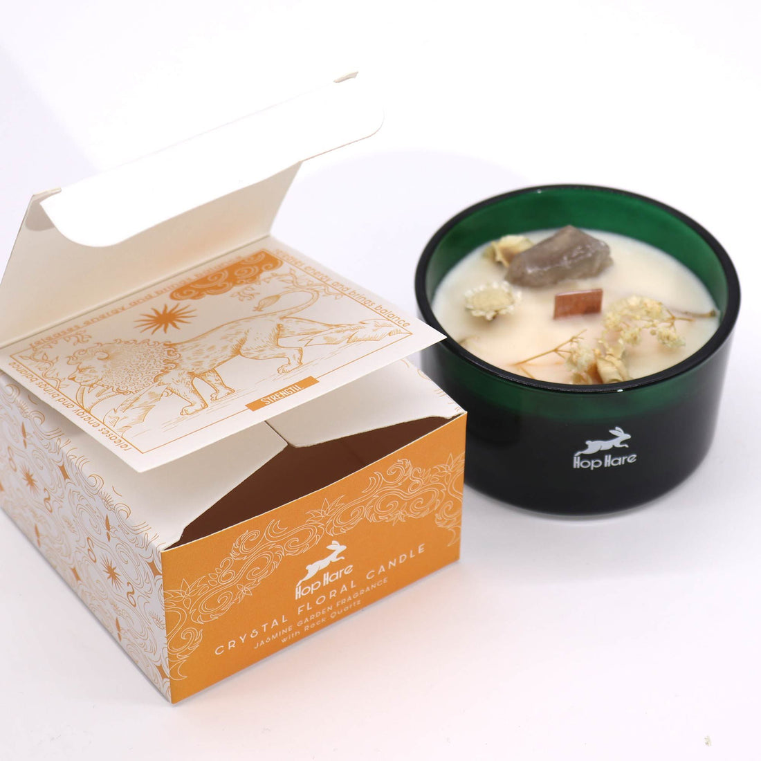 Candle in a dark green container with floral elements next to its packaging on a white background