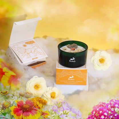 A candle displayed with a tarot card and orange gift box among bright flowers and golden clouds.